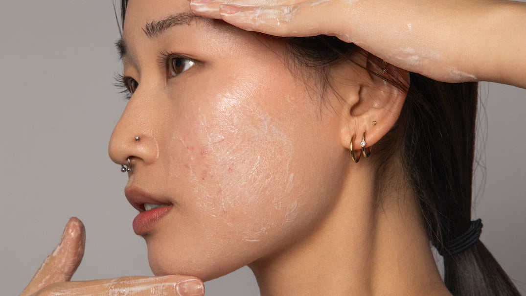 Woman with hands applying a skincare product to her face against a neutral background